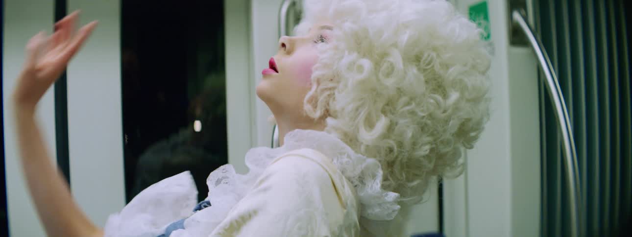 A woman dances on a train in a historical costume with a curly white wig