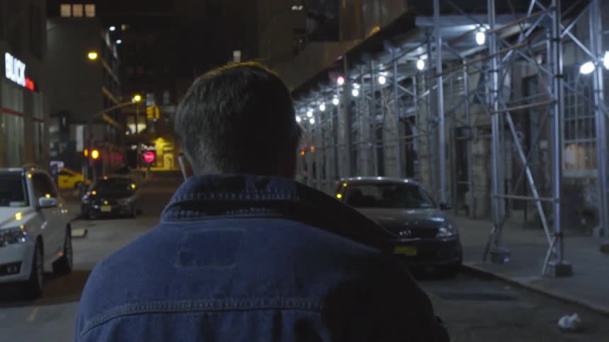 A man is walking down a street at night