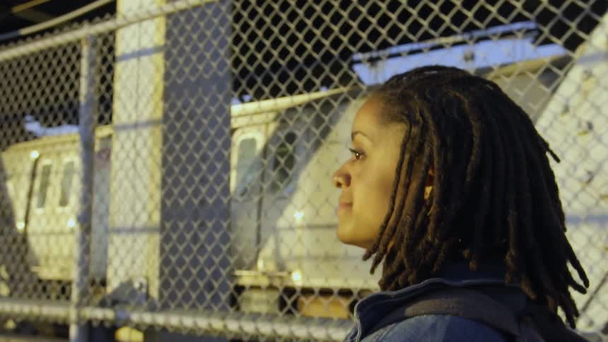 A woman is walking along a fence near a train