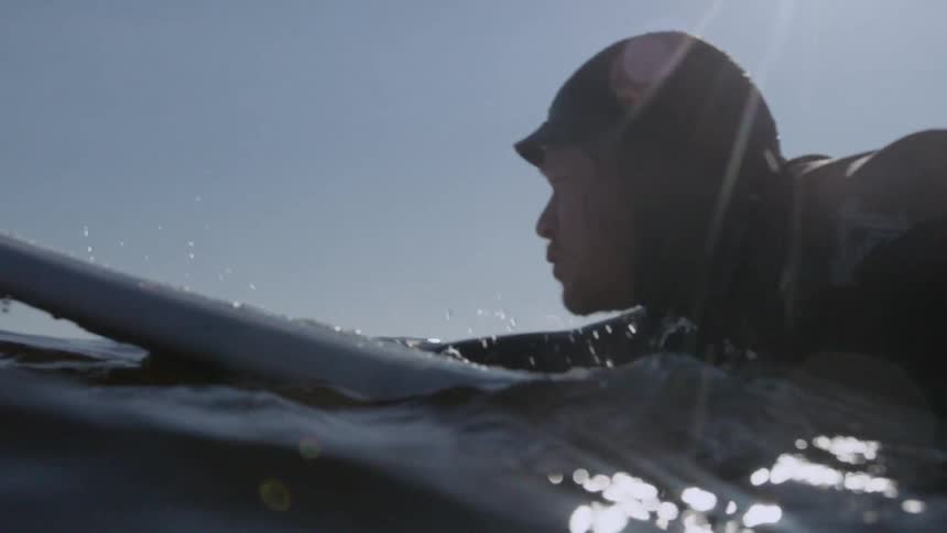 A man in a wetsuit paddles a surfboard through the water