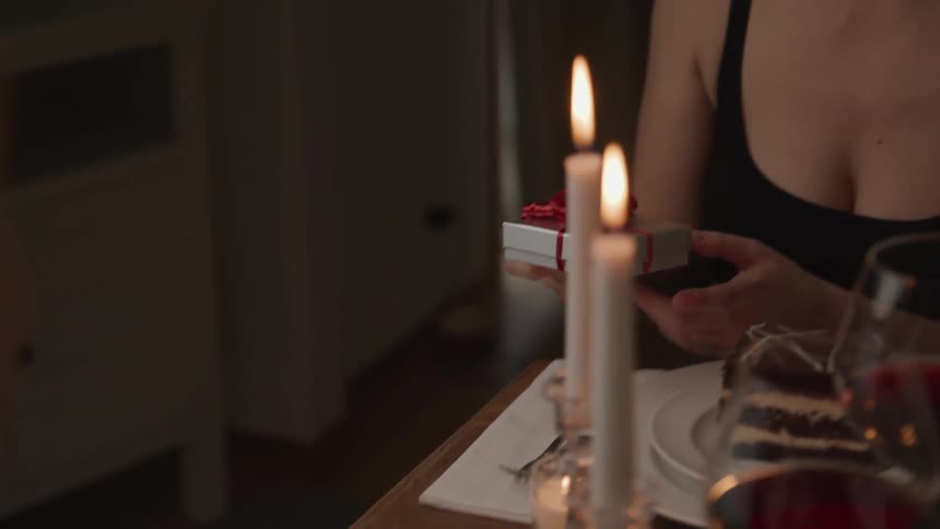 A woman picks up a gift box from a candle lit dinner table