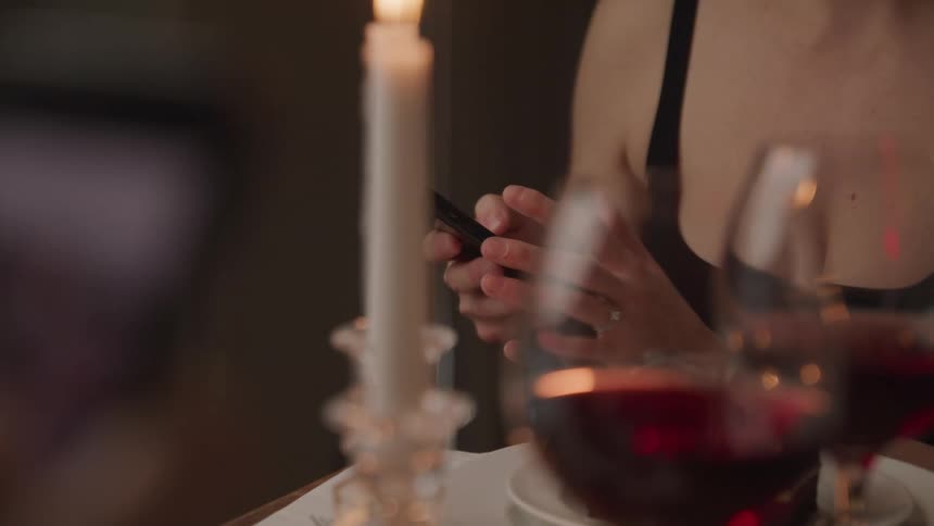 A woman uses her smartphone while sitting at a dining table covered in candles and wine glasses