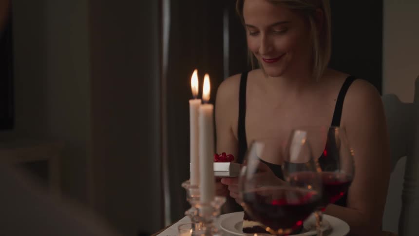 A woman sitting at a table with wine and dessert picks up a gift and smiles
