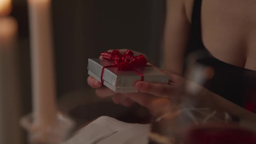 A woman sitting at a table with dessert and wine holds a gift in her hands