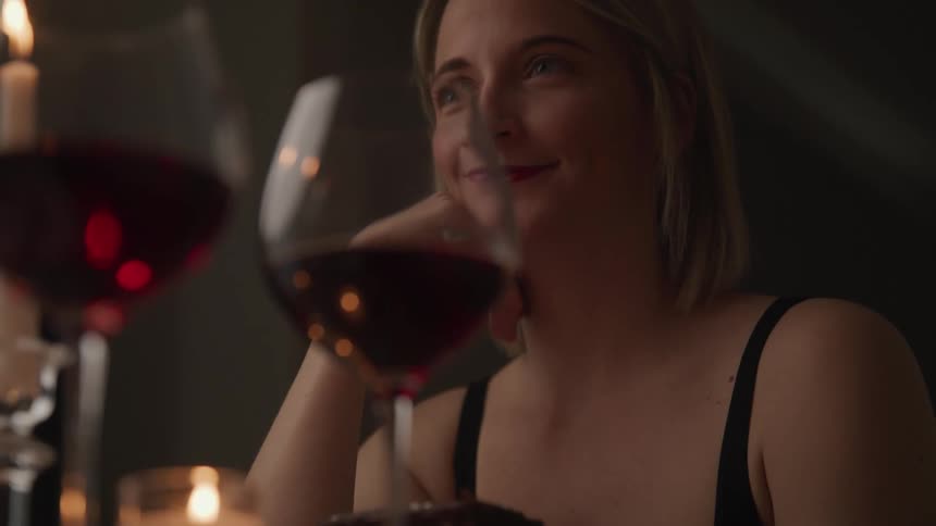 A woman at a table with candles and glasses of wine smiles at someone