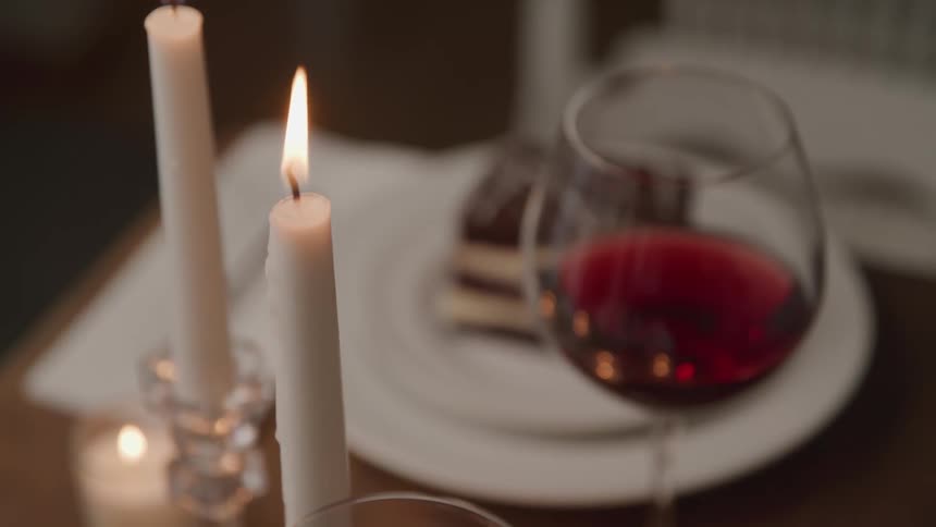 A glass of red wine and cake on a table during a candlelit dinner