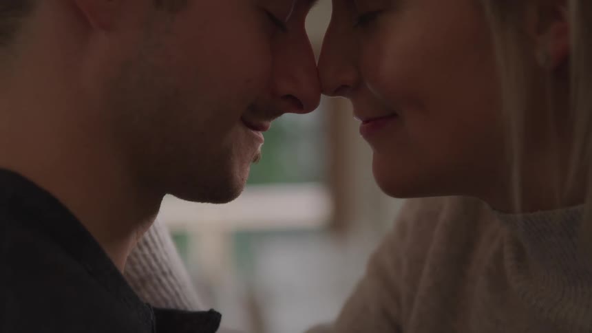 A man and woman embrace while pressing their foreheads and noses together