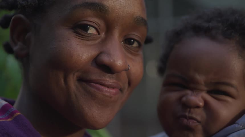 A woman smiles while holding a small child who is playfully making faces