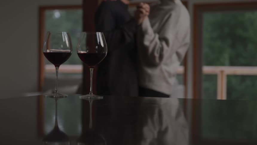 A pair of people dance together as two glasses of wine sit on a nearby counter