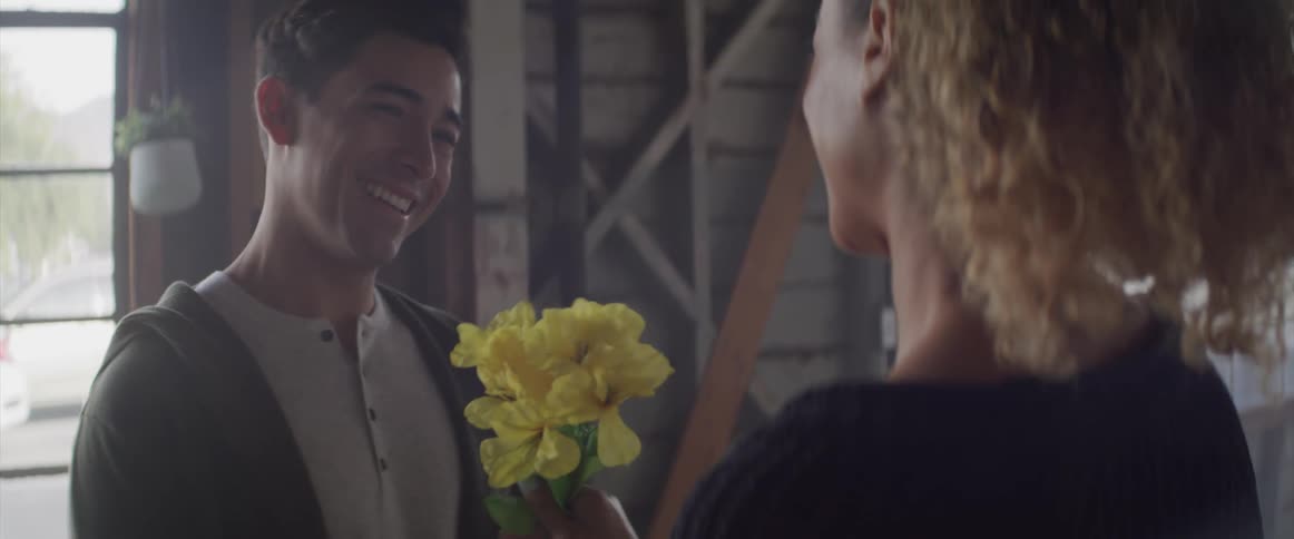 A couple hugging as the male hands the female flowers