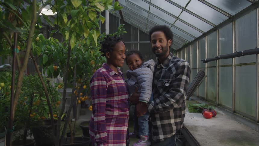 A family stand in their greenhouse near some crops