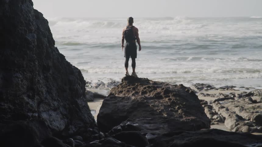 A male standing on a rock on a beach