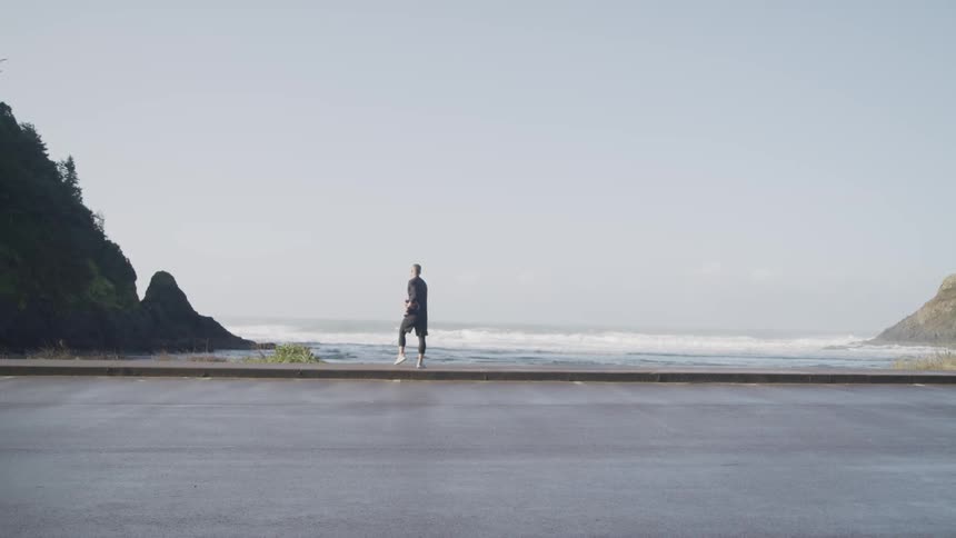 A man stretches on a sidewalk near the shore