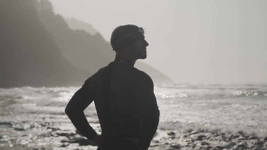 A man stands by the ocean edge looking toward the water