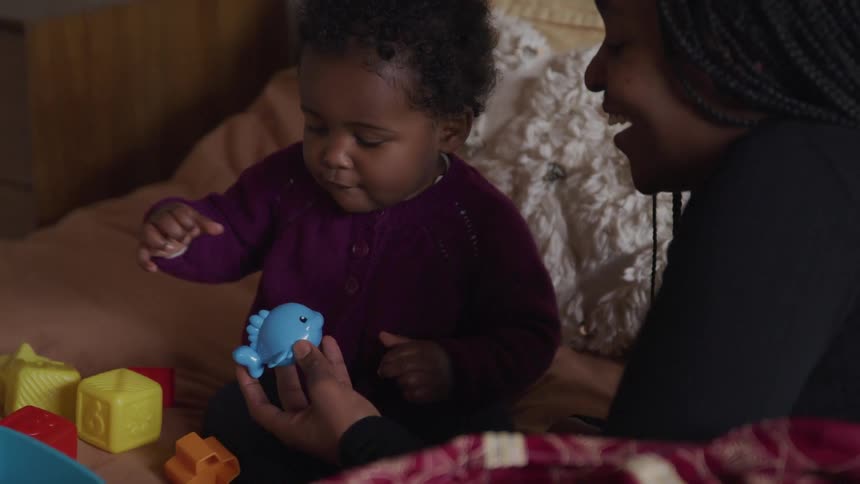 A mom smiles and laughs as she hands her baby daughter a toy