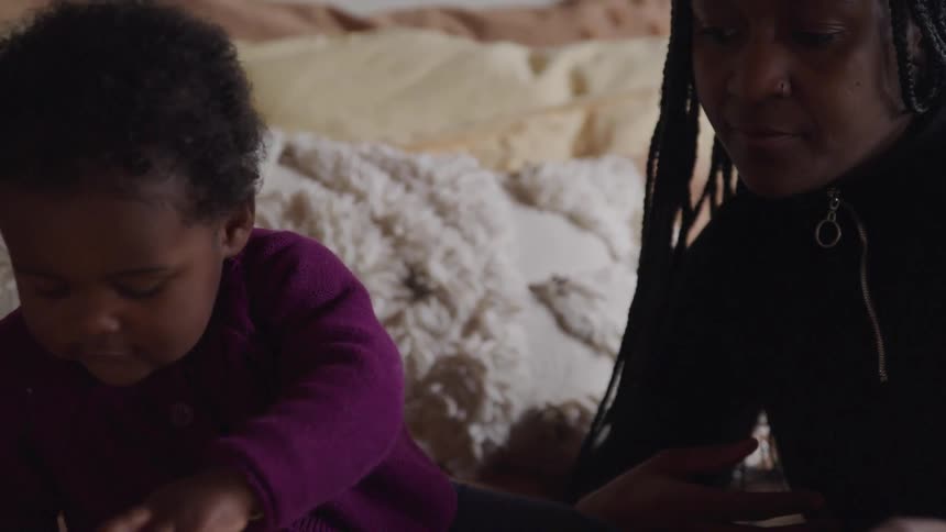 A woman and her infant play with toy blocks while sitting in bed