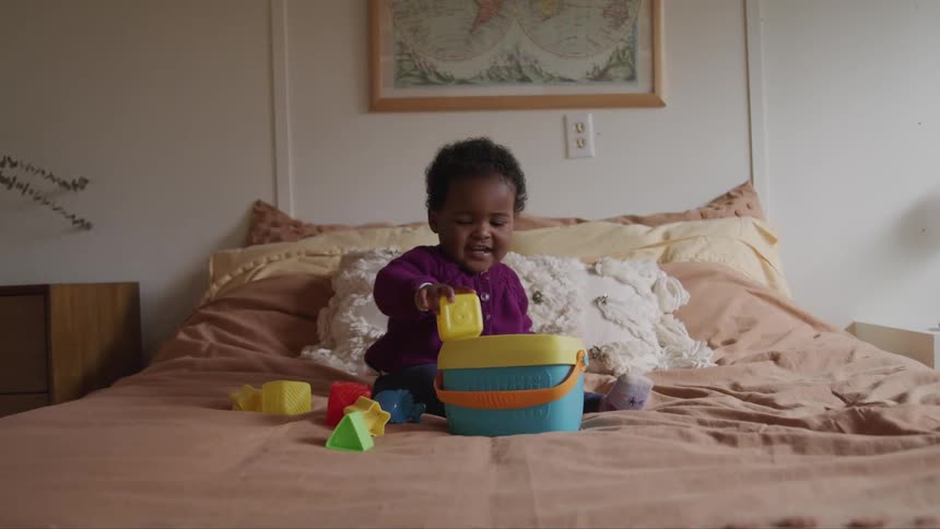 A baby sits on a bed and plays with a pile of blocks