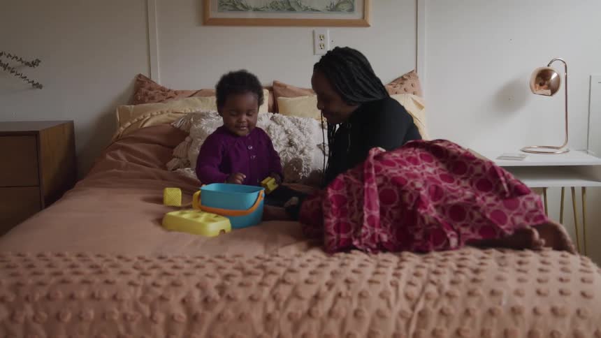 A mother lies on her bed at home and plays with her baby girl