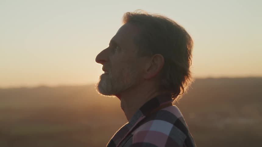 Man stands outdoors looking as sun on horizon casts them into silhouette