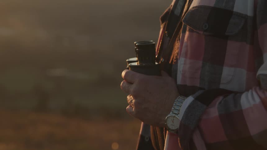A man stands outside and holds binoculars