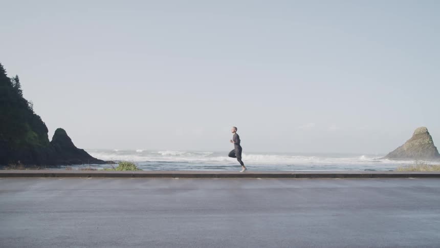 A man jogs along an empty beach right at the water edge