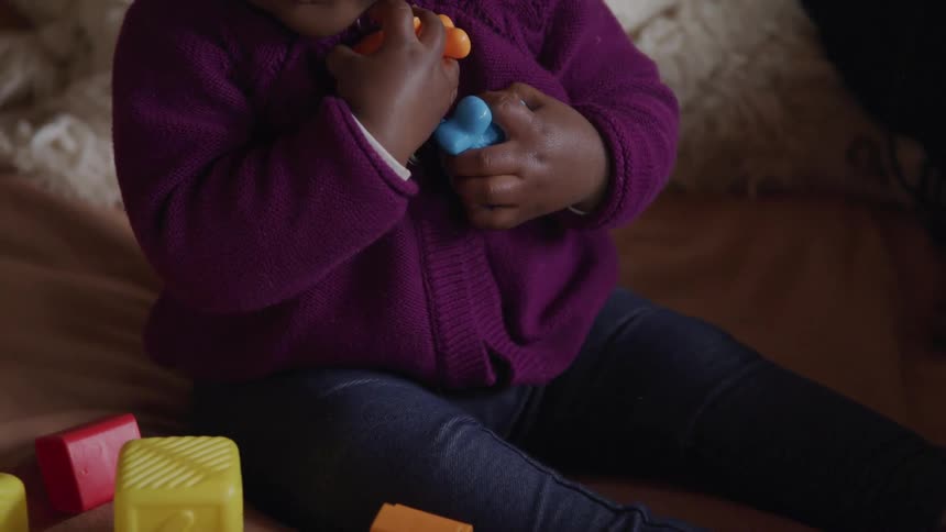 A small child sits on a bed clutching toys to their chest