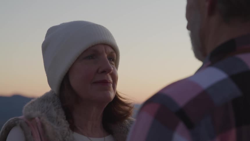 A man and woman are standing outdoors at dusk