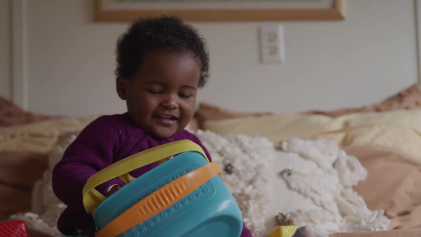 Black toddler laughs while pulling colored blocks out of a basket