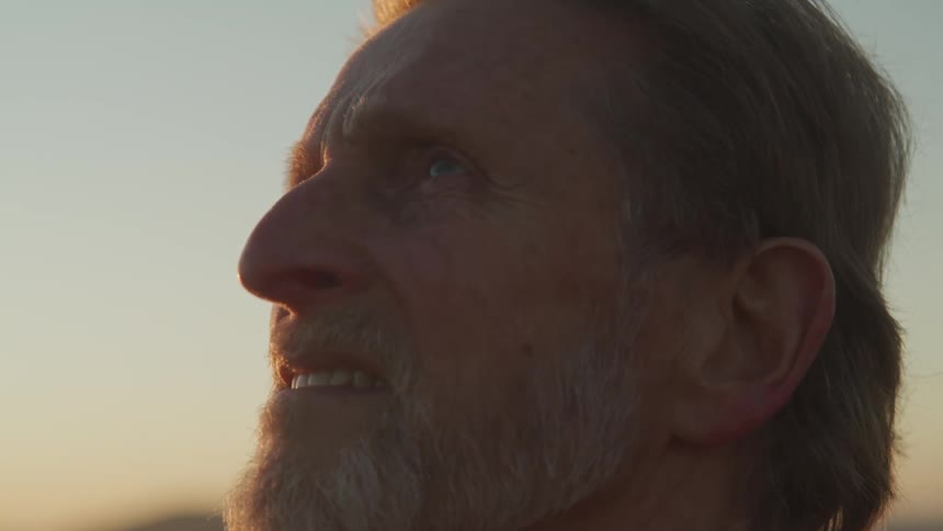 Side view of an elderly man with a grey beard looking up at sunset