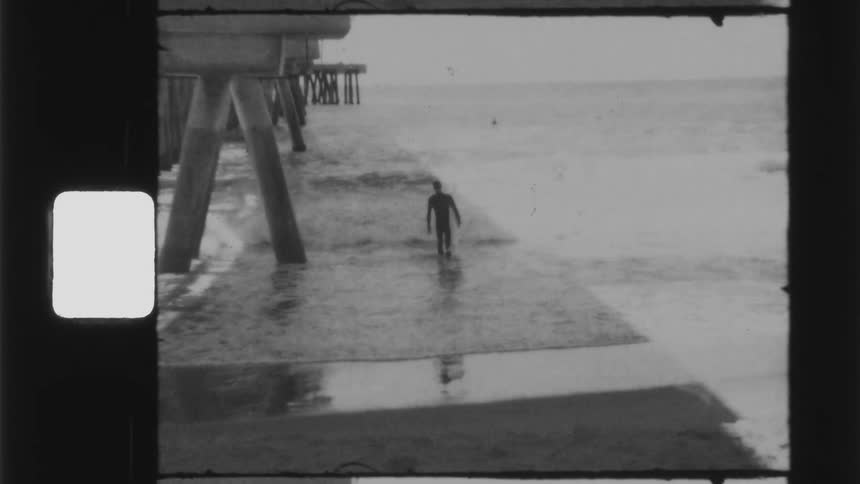 Vintage footage of a man walking in to the water by a pier