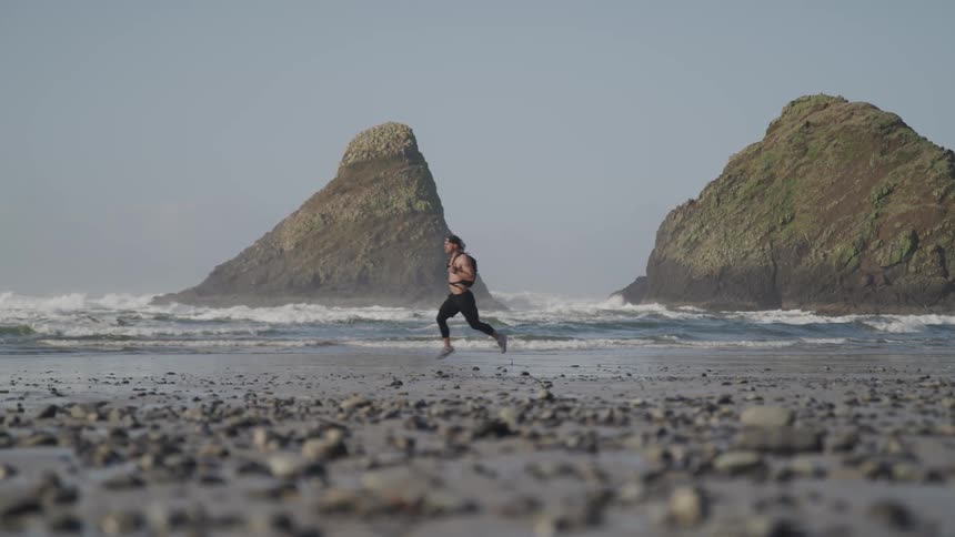 A man runs across the pebble stone beach at the ocean edge