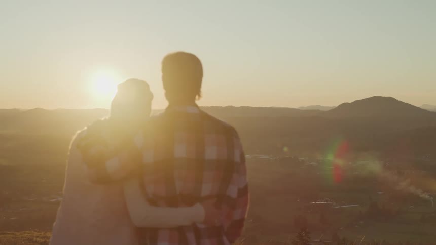 Young couple hugging atop a mountain at sunset