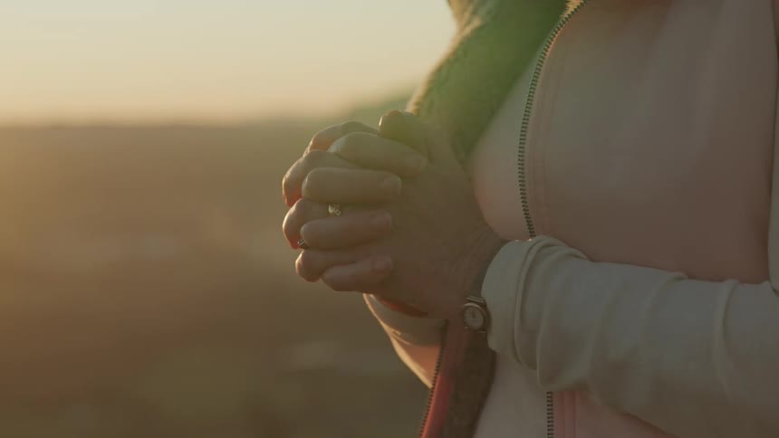 Woman prays standing outdoors as sun turns sky red