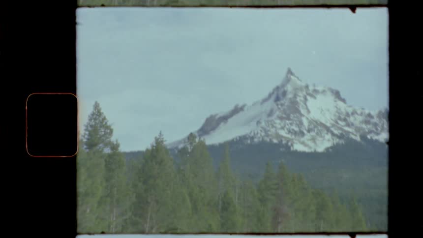 A car travels on a forest road with a snowy mountain peak in the distance