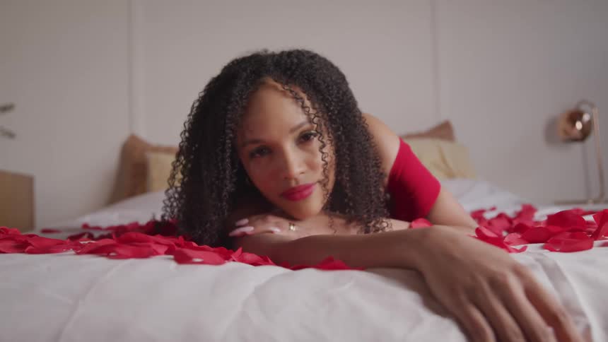 A woman in red lays seductively on a bed covered in red flower petals