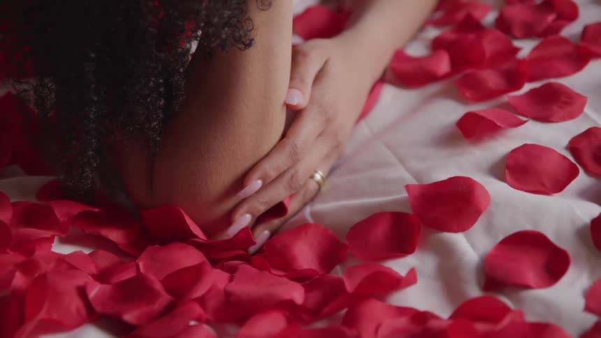 A woman is relaxing indoors on a bed covered with red rose petals