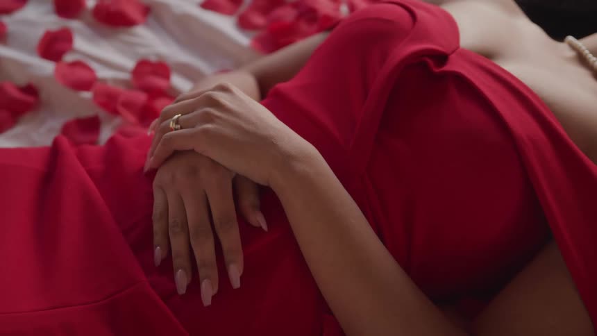 Woman in red formal gown laying on bed with rose petals