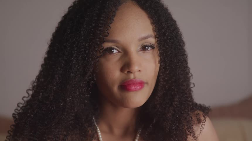 Black woman with curly hair and makeup looks at the camera with eye contact