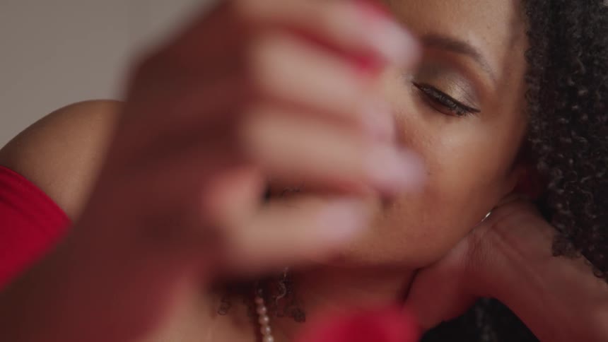Young woman wearing a red dress reclines in a bed playing with rose petals