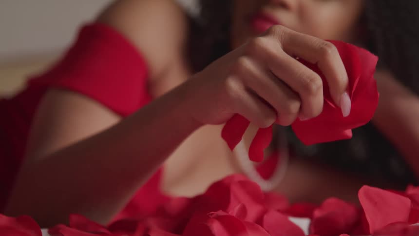 A young woman lies on a bed and picks up and drops flower petals