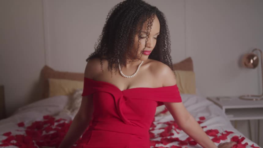 A woman is sitting on a bed full of rose petals