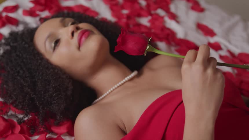 A woman lying on a bed of rose petals holding a rose