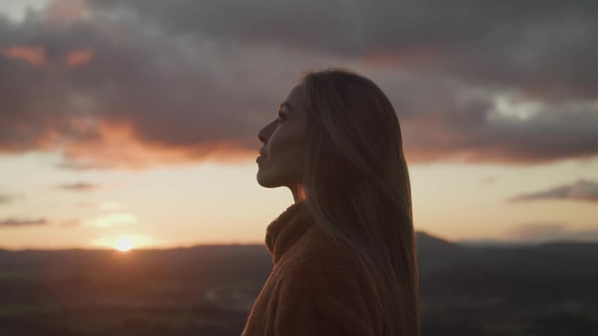 A woman is standing outdoors while the sun is setting