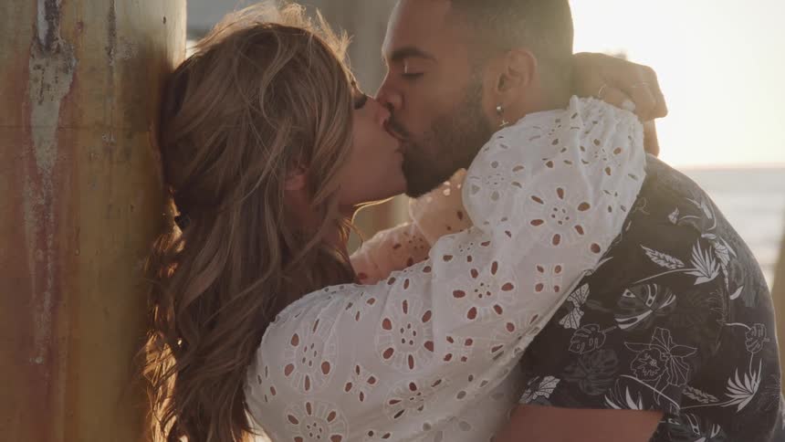 A man and woman are kissing outdoors at sunset