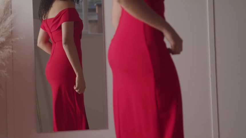Woman stands in red dress looking in mirror and adjusting dress