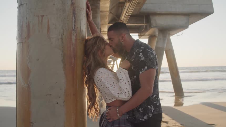 A man and woman kissing under a pier on the beach
