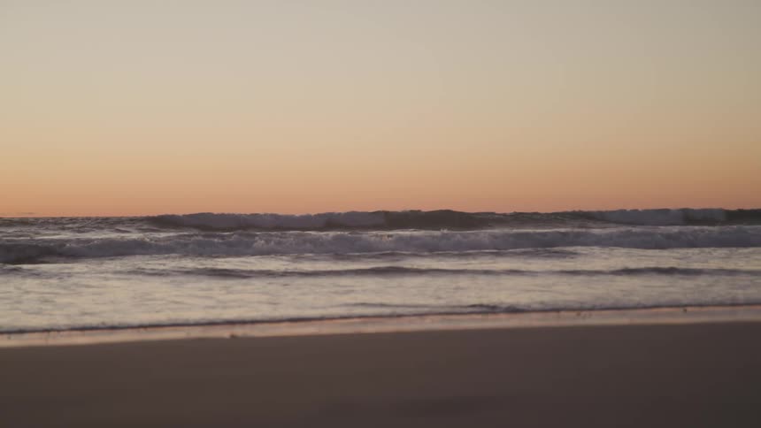 Waves roll into a sandy beach at sunset