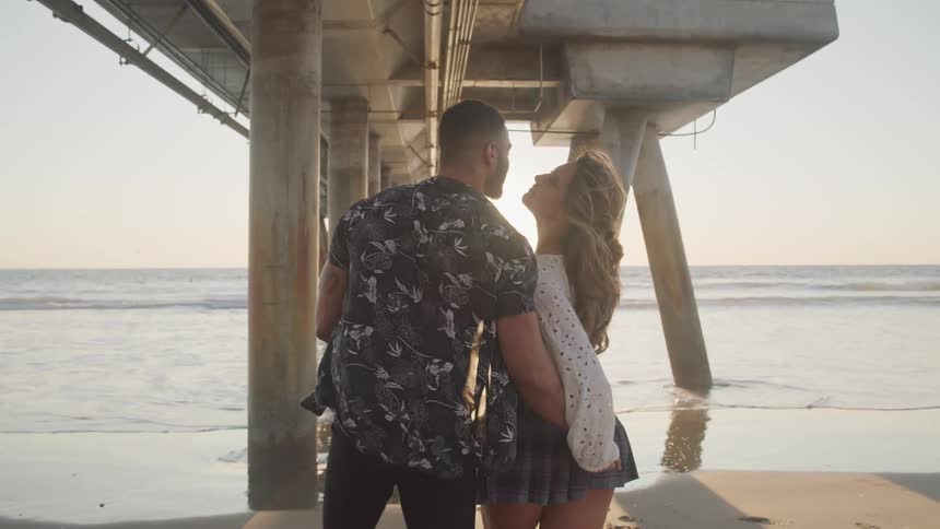 A man and woman are walking on the beach at dusk