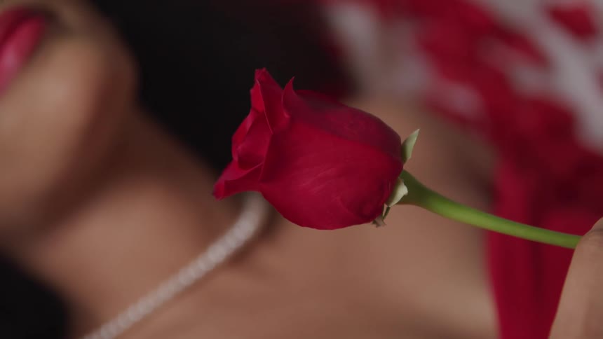 A woman lying on her back slowly spins a rose in her hand