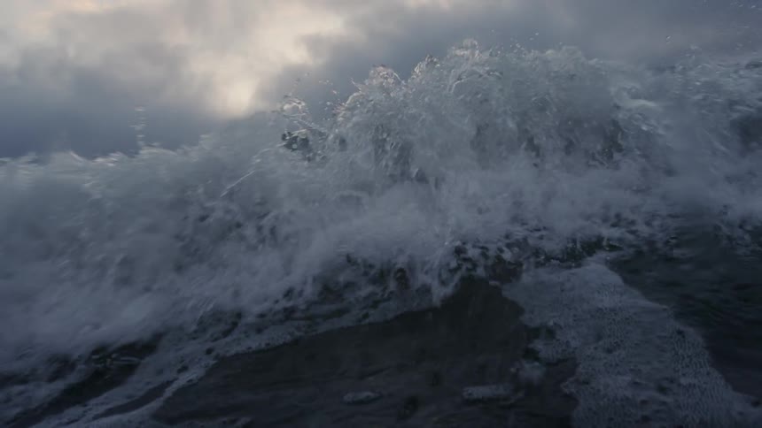 A large wave crashes on a cloudy day